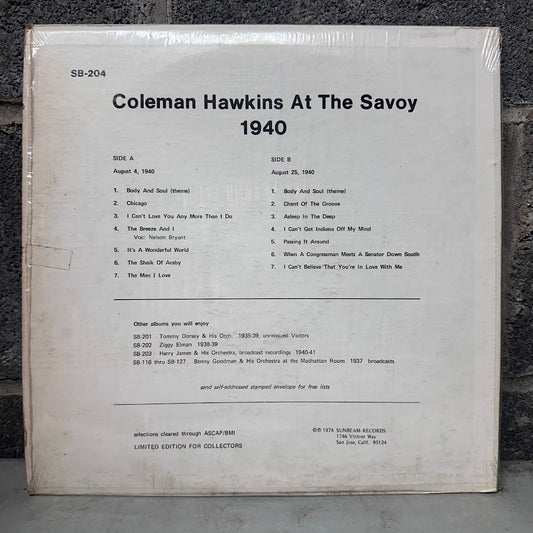 A square vinyl record sleeve or booklet cover for Coleman Hawkins 'At The Savoy 1940', photographed flat on a dark textured surface. The cover is off-white with black printed text listing track titles, side A and B, and additional catalog information.