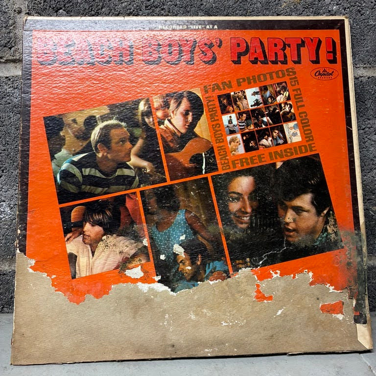 A vintage Beach Boys 'Party!' vinyl record album cover, showing orange artwork with multiple black-and-white and color photos of the band members, photographed on a gray textured surface.