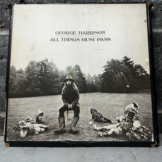 Album cover of 'All Things Must Pass' by George Harrison with a black and white photo of a man sitting on a stool with three people lying on the grass.