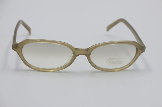 Oval eyeglasses with translucent olive-brown frames and clear lenses, featuring a visible Calvin Klein logo on the lower right lens, set against a plain light gray background.