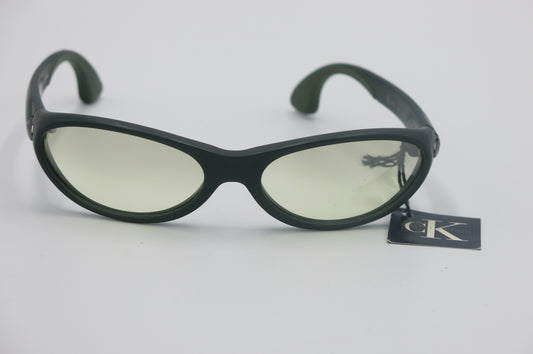 Black cat-eye sunglasses with light yellow tinted lenses and a black CK tag attached, photographed on a light gray background.