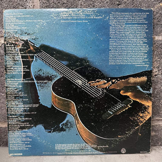 The back cover of a vinyl record sleeve for Janis Joplin's album 'Blowout', featuring a distressed blue and black background with a large acoustic guitar graphic and track listing text. Released on MCA Records.