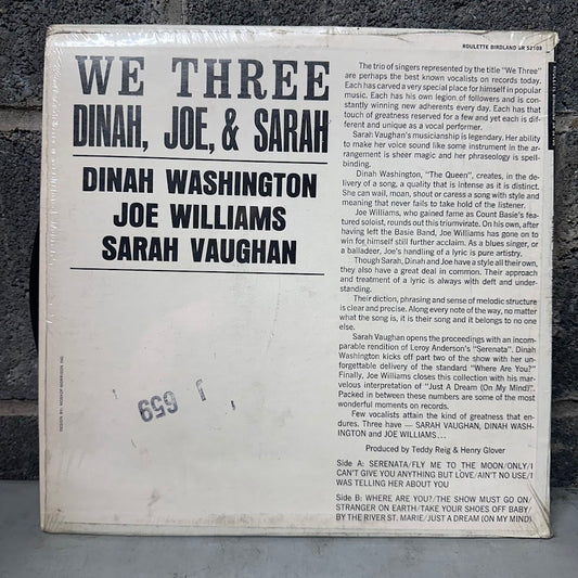 A vintage music print or album cover insert for 'We Three Dinah, Joe, & Sarah' by Joe Williams and Sarah Vaughan, featuring large black title text and multiple columns of printed text on a white background, photographed outdoors on dark gravel.