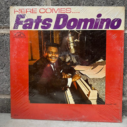 Vinyl record cover featuring Fats Domino sitting at a piano with text 'Here Comes Fats Domino' on a textured surface.