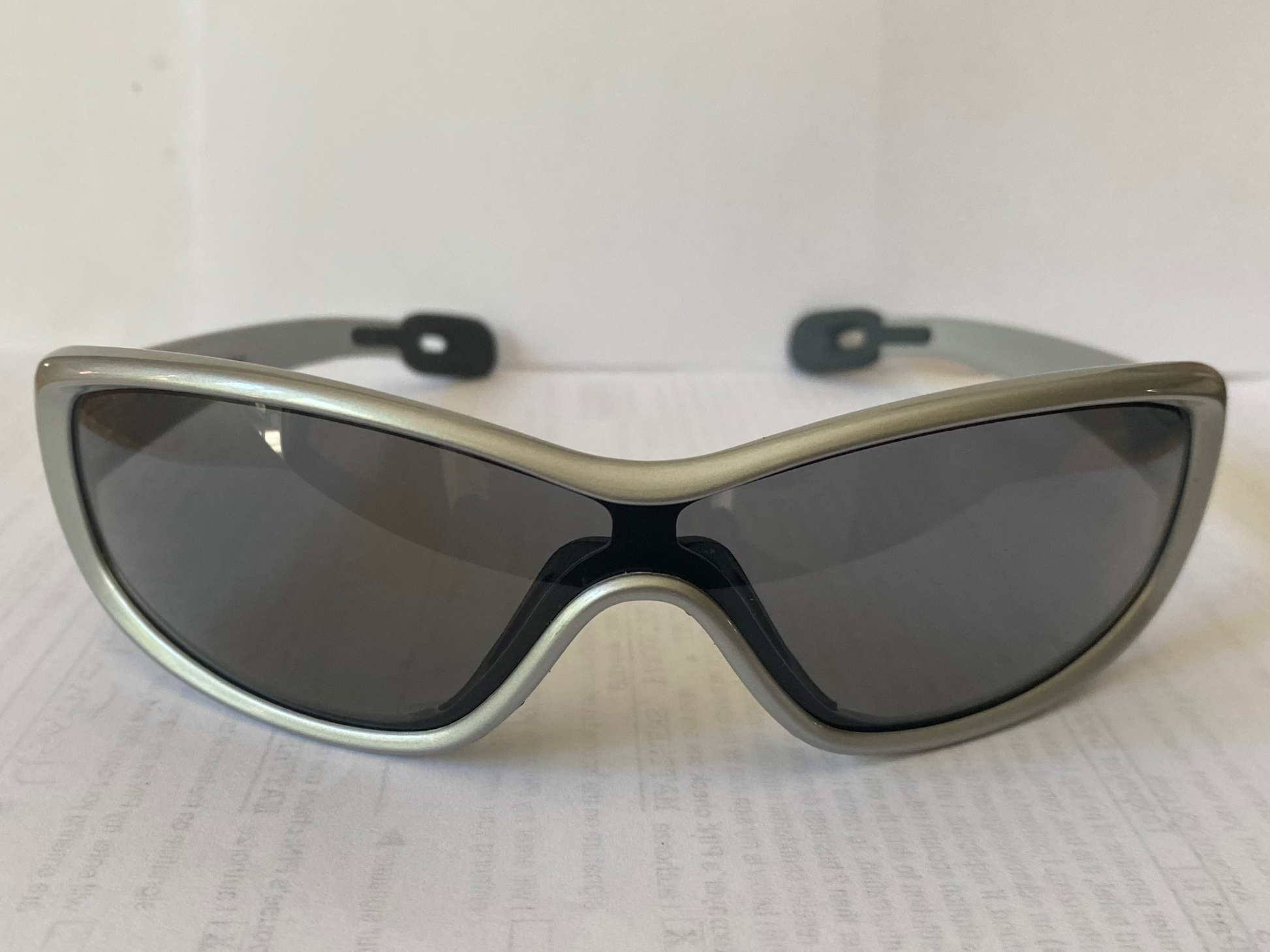 Sunglasses with a silver frame and dark lenses on a white sheet of paper.